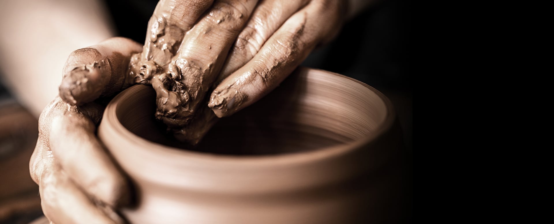 Mains d'un potier couvertes de terre cuite façonnant avec concentration un vase sur un tour en rotation.